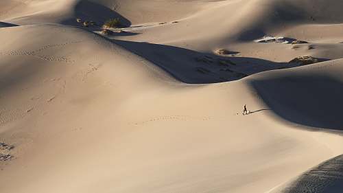 brown person walking alone in middle of desert dune